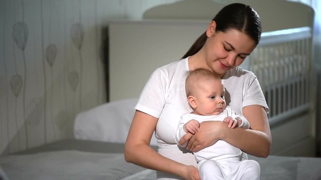 Mom nursing baby. Woman and new born boy relax in a white bedroom. Family at home.