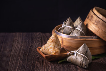 Obraz na płótnie Canvas Rice dumpling, zongzi - Bunch of Chinese traditional cooked food on wooden table over black background, concept of Dragon Boat Festival, close up, copy space