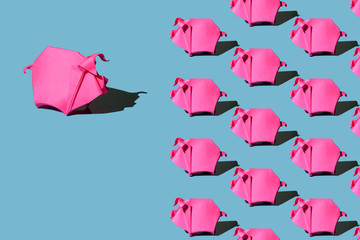 One big origami pink paper pig in front of many small paper pigs on blue background with hard shadow © Elena Simonova