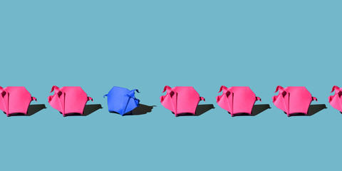 One blue paper pig stands out in the ranks of other pink paper pigs on blue background with hard shadow