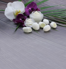 Fototapeta na wymiar Vertical web banner with jars of cosmetic cream, silkworm cocoons, orchids and a palm leaf on a dark wooden background with a brightened place for text.