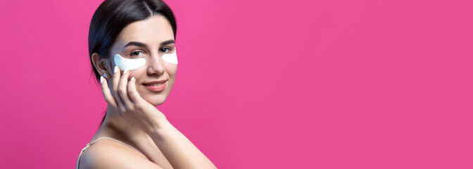 Close up portrait of pretty attractive girl with naked shoulders using patches under eyes. Standing over pink background.