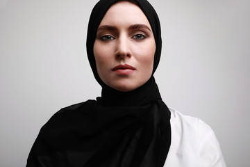 Close-up portrait of young beautiful muslim woman in hijab. Isolated over white wall.