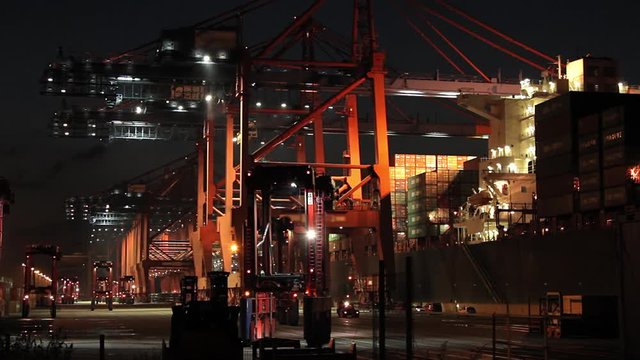 Container ship loading and unloading at night in the port of Hamburg. Waiting vehicles in front with flashing yellow warning lights