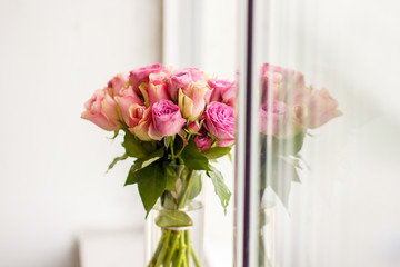 vase of flowers on a windowsill, a bouquet of pink roses on long stems with leaves
