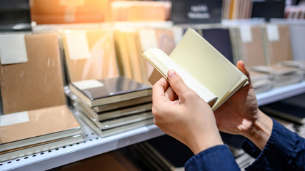 Male hand customer choosing new paper notebook from display rack in stationery shop. Buying office supply concept