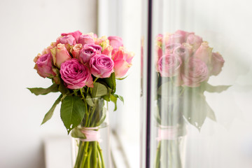 
a vase of flowers on the windowsill, reflected in the window, bright pink roses on the long stems
