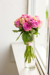 
a vase of flowers on the windowsill, reflected in the window, bright pink roses on the long stems
