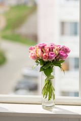 Fototapeta na wymiar transparent vase with a bouquet of roses in a window with a city view