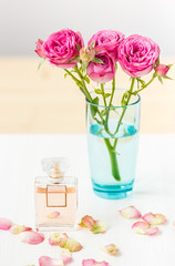a sprig of spray roses in a glass on a table with perfume