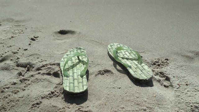 Men's slippers on the beach washed by water