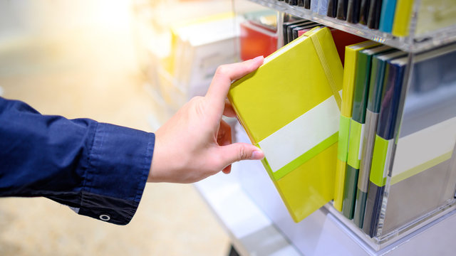 Male Hand Customer Choosing New Yellow Paper Notebook From Display Rack In Stationery Shop. Buying Office Supply Concept