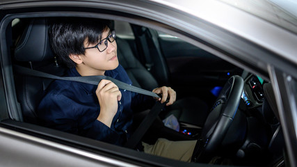 Fototapeta na wymiar Driving safety concept. Asian businessman fasten seat belt while sitting on driver seat in modern car. Land vehicle for urban lifestyle.
