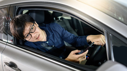 Fototapeta na wymiar Driving safety concept. Car insurance for urban lifestyle. Asian business man open auto door mirror looking outside of modern car and using smartphone phone while driving car.