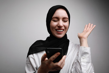 Young muslim woman sending audio voice message on cellphone talking to mobile assistant. Wearing black hijab.