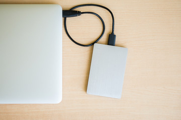 External hard drive connect to laptop computer on wooden background