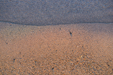 Sea wave and sand seashore. Golden sun light over the sea ocean waves. MIrror reflection on water surface. Macro close up.