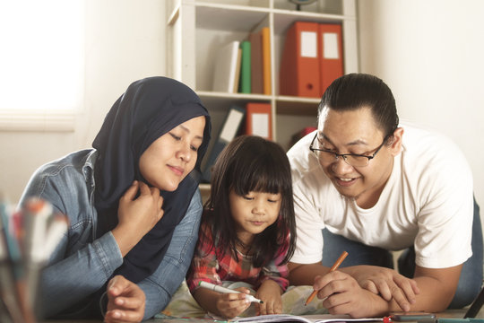 Asian muslim parents drawing with their daughter, mother and father teaching baby girl, happy family concept