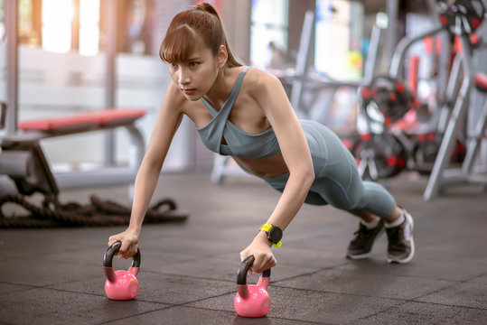 Fitness woman workout with kettlebell training and Doing plank on kettlebell. Push-up on weights in the gym .