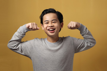 Portrait of funny strong healthy Asian boy shows his muscle and strength, confident kid shows his...