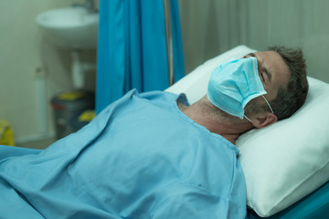attractive and scared man infected by covid-19 - dramatic portrait of adult male in face mask receiving treatment at hospital suffering respiratory disease lying on bed worried