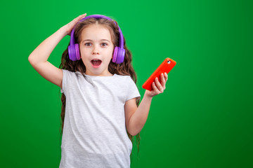 little girl in headphones with a phone in her hands on a green background in studio