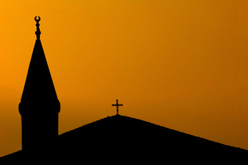 The islamic 'crescend moon'-symbol on a mosque, together with the christian cross on a church,during sunset in Istanbul,Turkey.A concept of coexistence or hostility and terrorism between two religions © Thomas