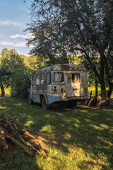 Old rusty soviet bus in a wild forest with an abandoned house