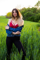 A girl in denim clothes with beautiful hair stands on a green field with a dreamy look on her face. Warm spring day