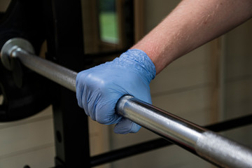 Rubber gloves being worn in a gym to lift weights and avoid diseases like coronavirus, the metal barbell could have traces of covid-19