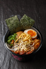 Asian noodle soup, ramen with pork, tofu, kimchi, vegetables and egg in black bowl. Slate background. Top view. Bowl of asian style soup. Japanese cuisine. Top view. Banner. Asian food