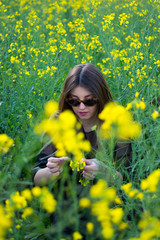 Girl in dark clothes with beautiful hair sitting in a field of yellow rape. Warm spring day