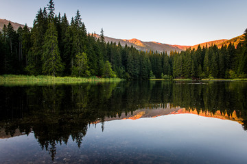 Beautiful landscape with mountains illuminated, reflection in mountain lake, blue sky and yellow sunlight. Slovakia, Vrbicke Pleso