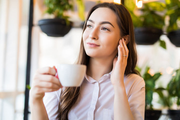 Smiling young woman at the cafe with headphones listening to music or talking on the phone