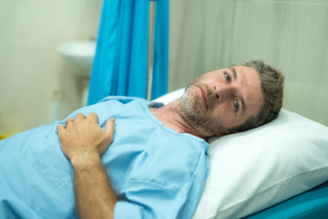 Obraz premium scared and worried man hospitalized - attractive injured man lying on hospital bed receiving treatment feeling sick after suffering accident or serious disease like cancer