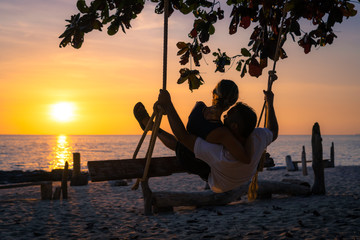 Couple on a swing at sunset in the beach.