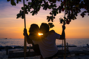 Kissing couple on a swing at sunset in the beach.