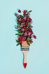Bristle painting brush with various berries, flowers and leaves on pastel blue background