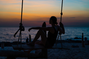 Young woman at dusk sitting on a swing.