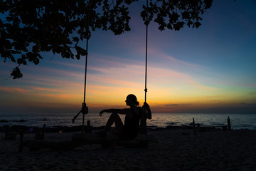 Girl on a swing at sunset in the beach. Silhouette.