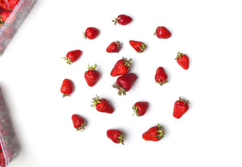 Top view of fresh tasty strawberries in plastic container and several strawberries separately circle forming on white backround. Summer time concept