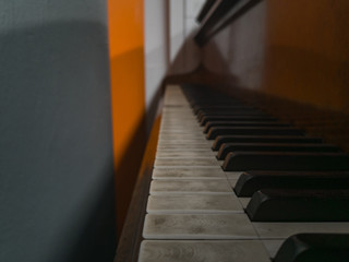 Old unused piano standing next to gray and orange wall