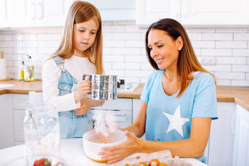 An attractive smiling family of mother daughter baking in a light kitchen at home.