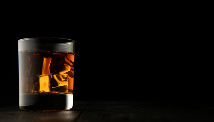 A glass of whiskey, which stands on a wooden surface, on a black background. CLose up