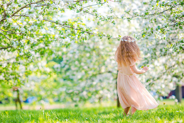Naklejka na ściany i meble Adorable little girl in blooming apple garden on beautiful spring day