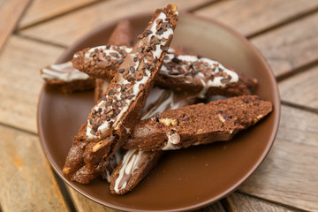 chocolate homemade biscotti cookies with white and dark chocolate on a brown plate on a wooden table