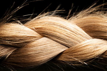 Healthy, shiny hair is braided on a black background. Hair sample.