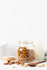 Oat granola with a bottle of milk, nuts and dried fruits to prepare a healthy breakfast on a bright kitchen table. Scandinavian white style. Selective focus.