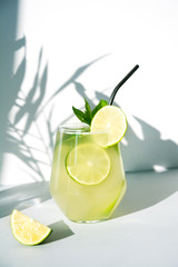 Fototapeta premium Freshness beverage with lime in glass garnish mint on white background with sunny shadow. Summer healthy drink. Vertical.
