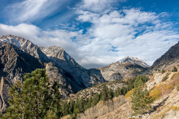 Fototapeta premium Dramatic clouds over snowy, high mountain peaks viewed from a valley filled with pine and aspen trees, Lundy Canyon, California
